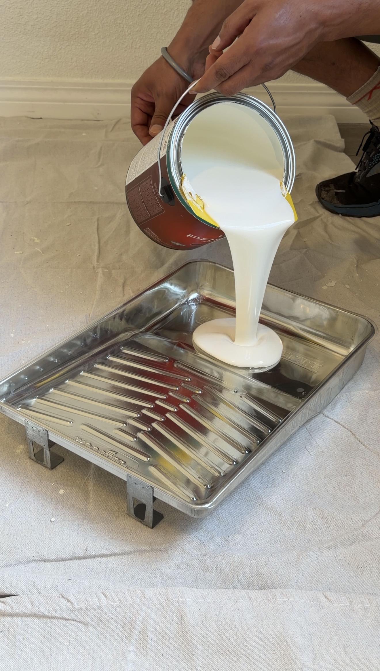 White paint being poured into a roller tray during the apartment painting project
