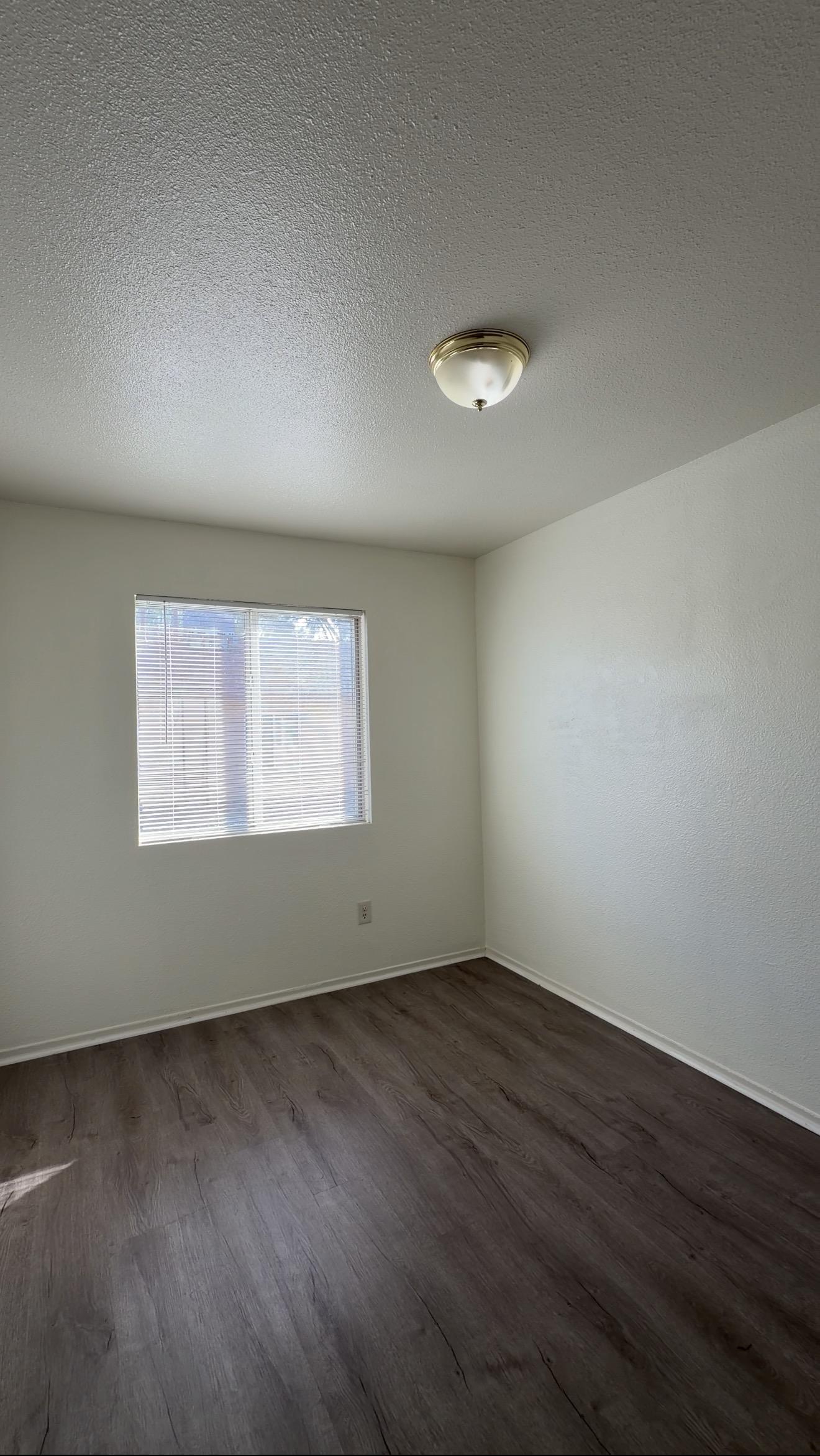 A refreshed empty room with light walls, a window, and wood-look flooring in the Bakersfield rental