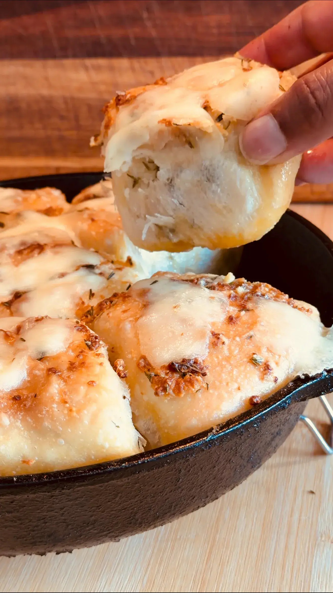 A hand lifting warm garlic bread from a cast-iron pan