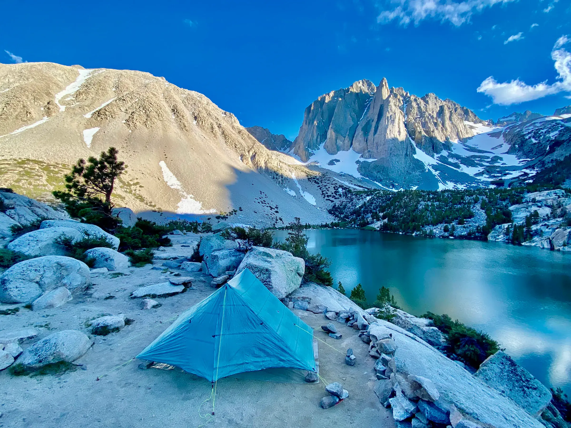 A backpacking tent pitched beside an alpine lake beneath snow-streaked Sierra peaks