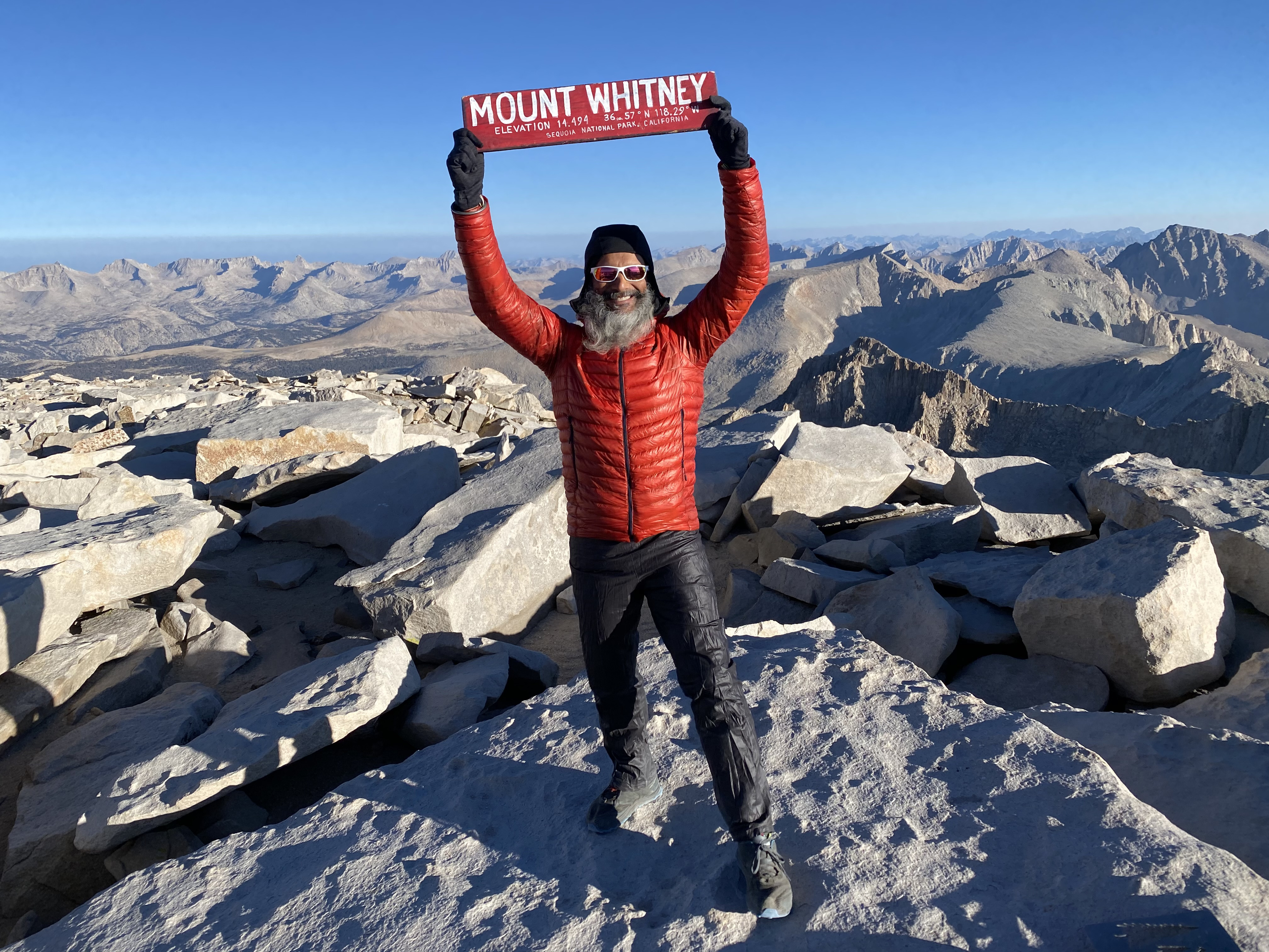 Gurpreet holding the Mount Whitney summit sign above the Sierra Nevada